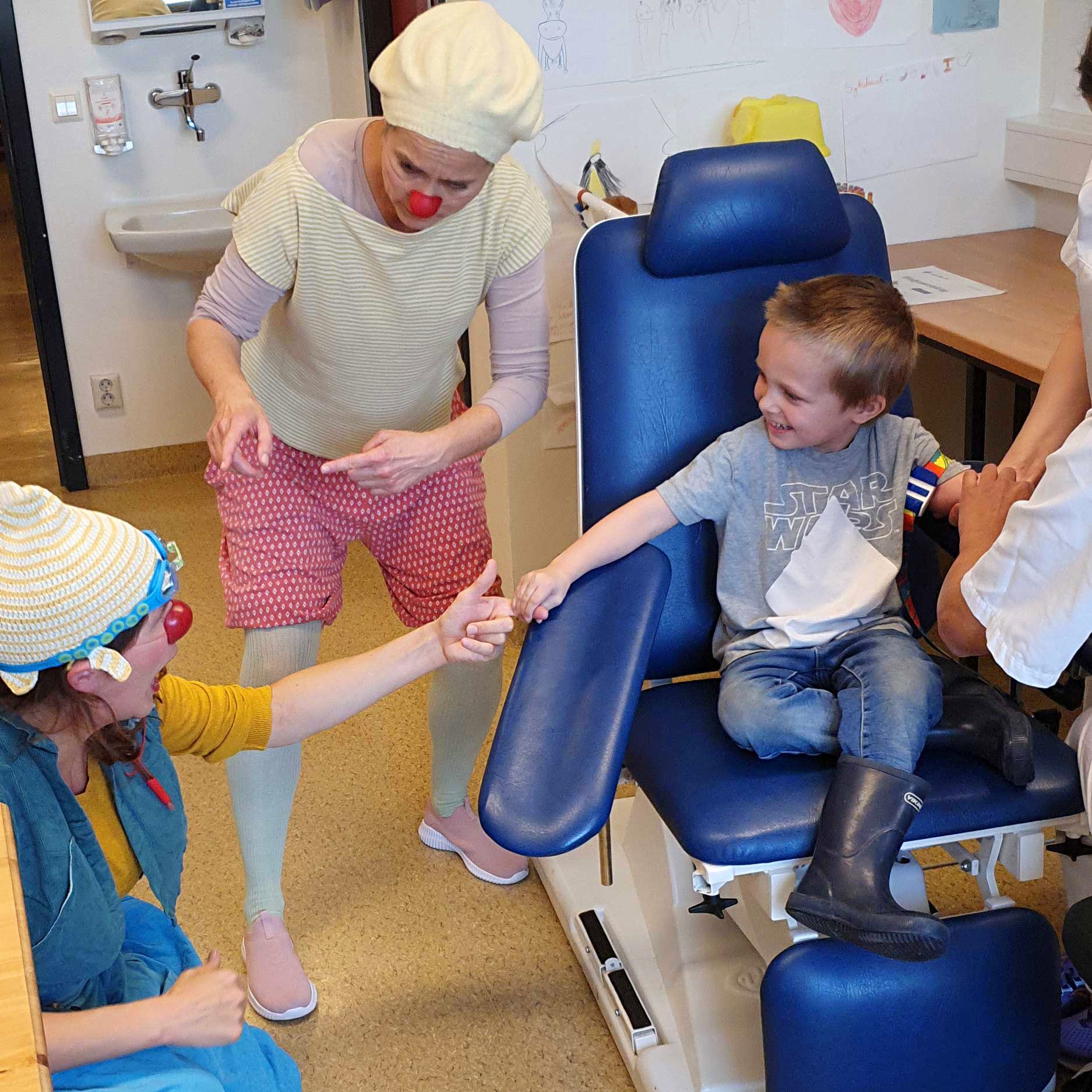 En liten gutt blir underholdt av sykehusklovner mens han tar blodprøve